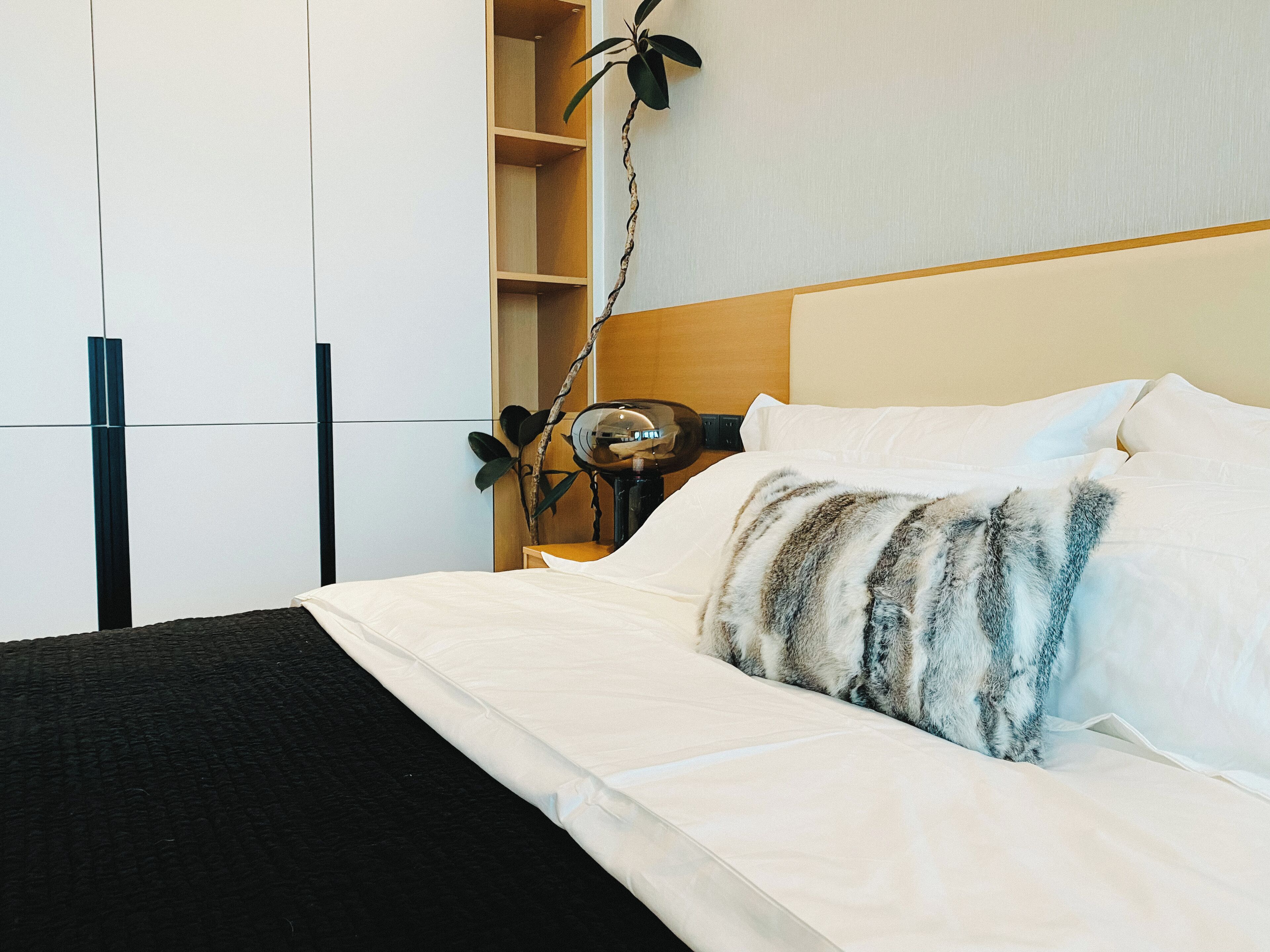 Et hotelværelse med seng, natbord, lampe, plante og garderobeskab.