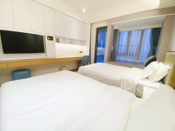Quarto de hotel com duas camas, uma escrivaninha, uma cadeira, televisão e janela com cortinas.