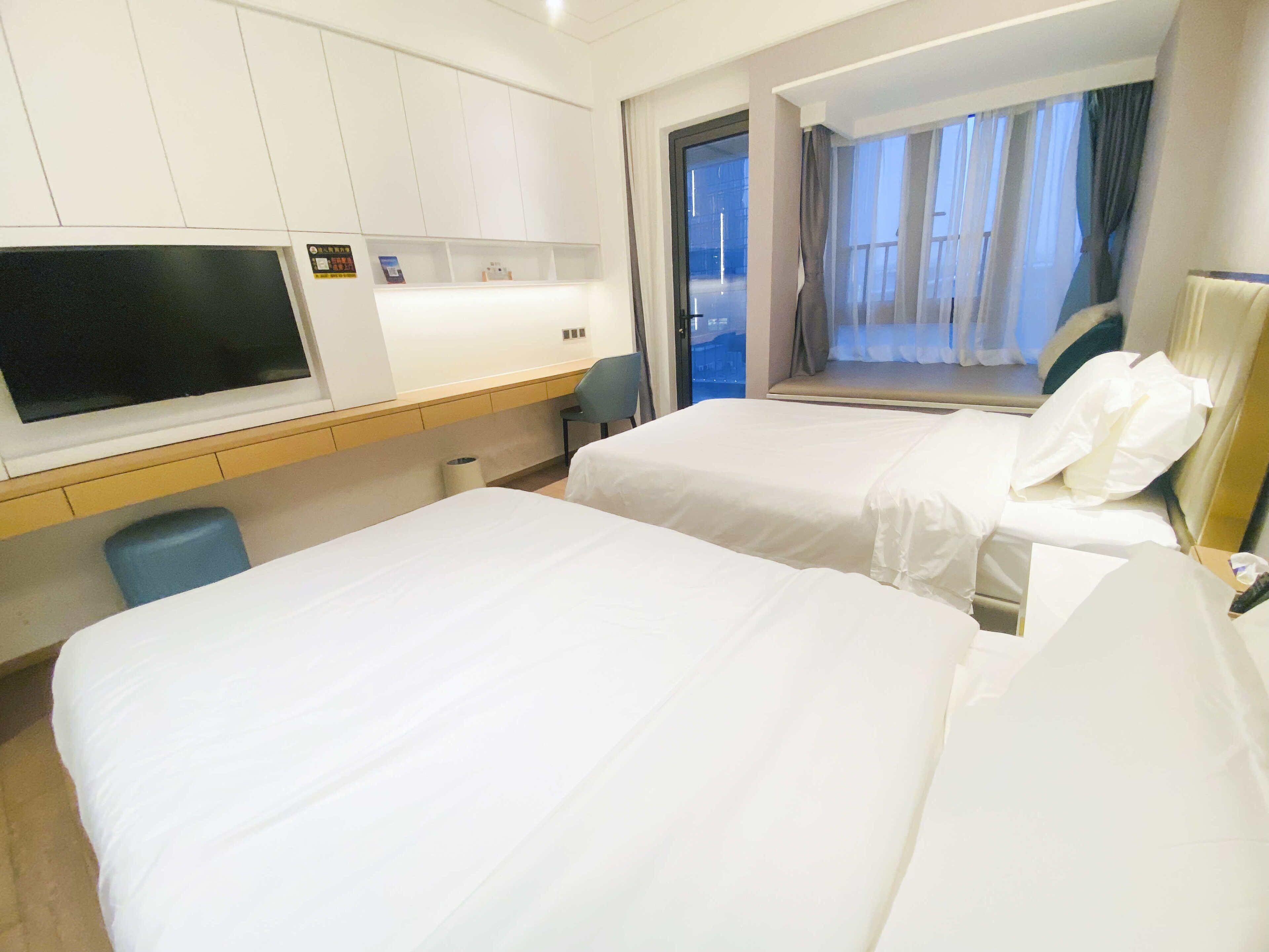 Une chambre d’hôtel avec deux lits, un bureau avec un téléviseur à écran plat, une fenêtre avec des rideaux et une vue sur l’extérieur.