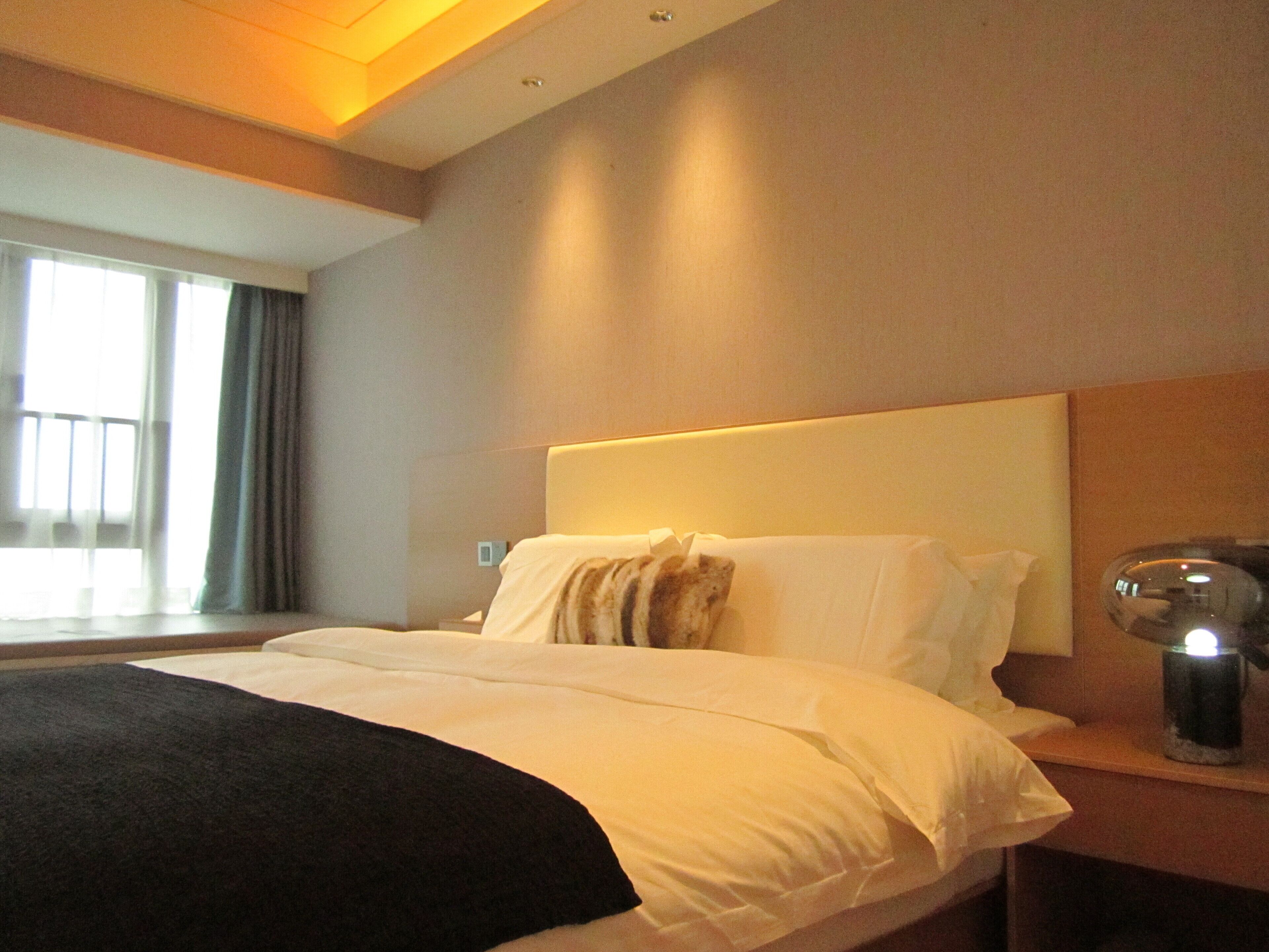 A hotel room with a large bed, a bedside table with a lamp, and a window with curtains.