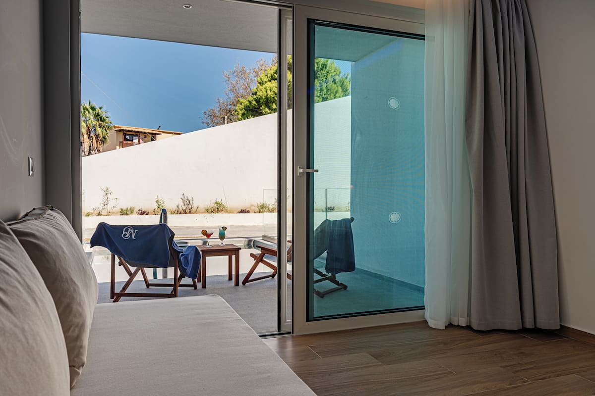 A modern hotel room with a sliding glass door leading to an outdoor area, a sofa, a small table, and a chair.