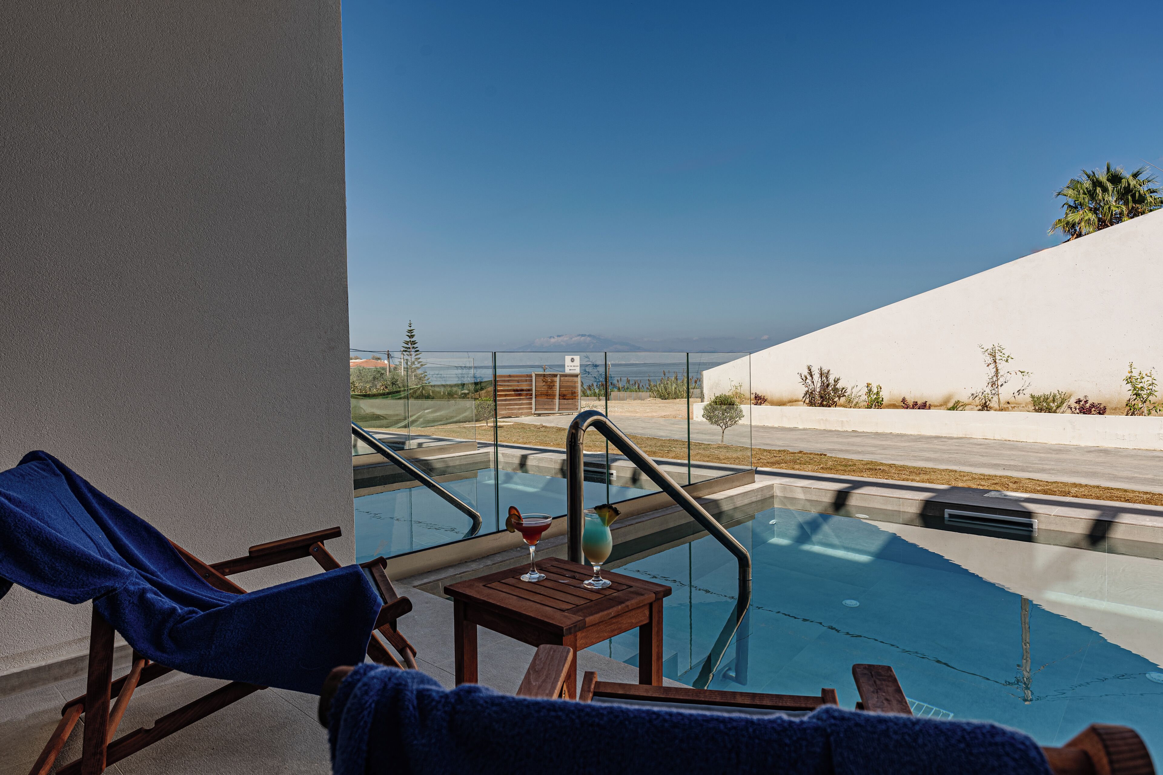 A pool area with lounge chairs and a table, overlooking a beach and ocean.