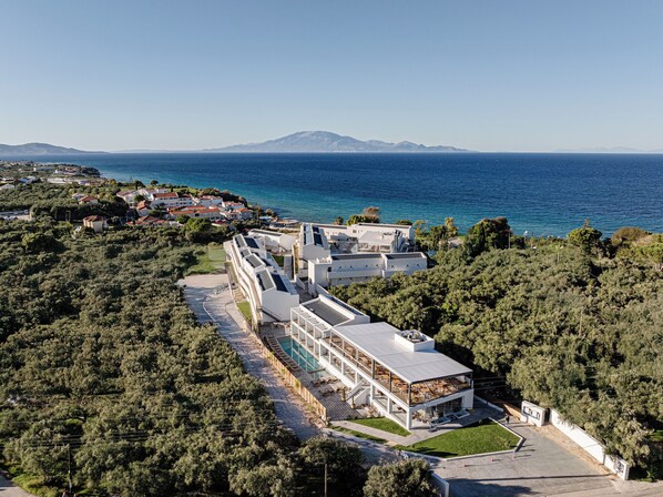 A modern hotel with a long, linear structure, surrounded by lush greenery and overlooking a coastal area with a clear view of the sea and distant mountains. - Magique Bleu Suites (Zakynthos)