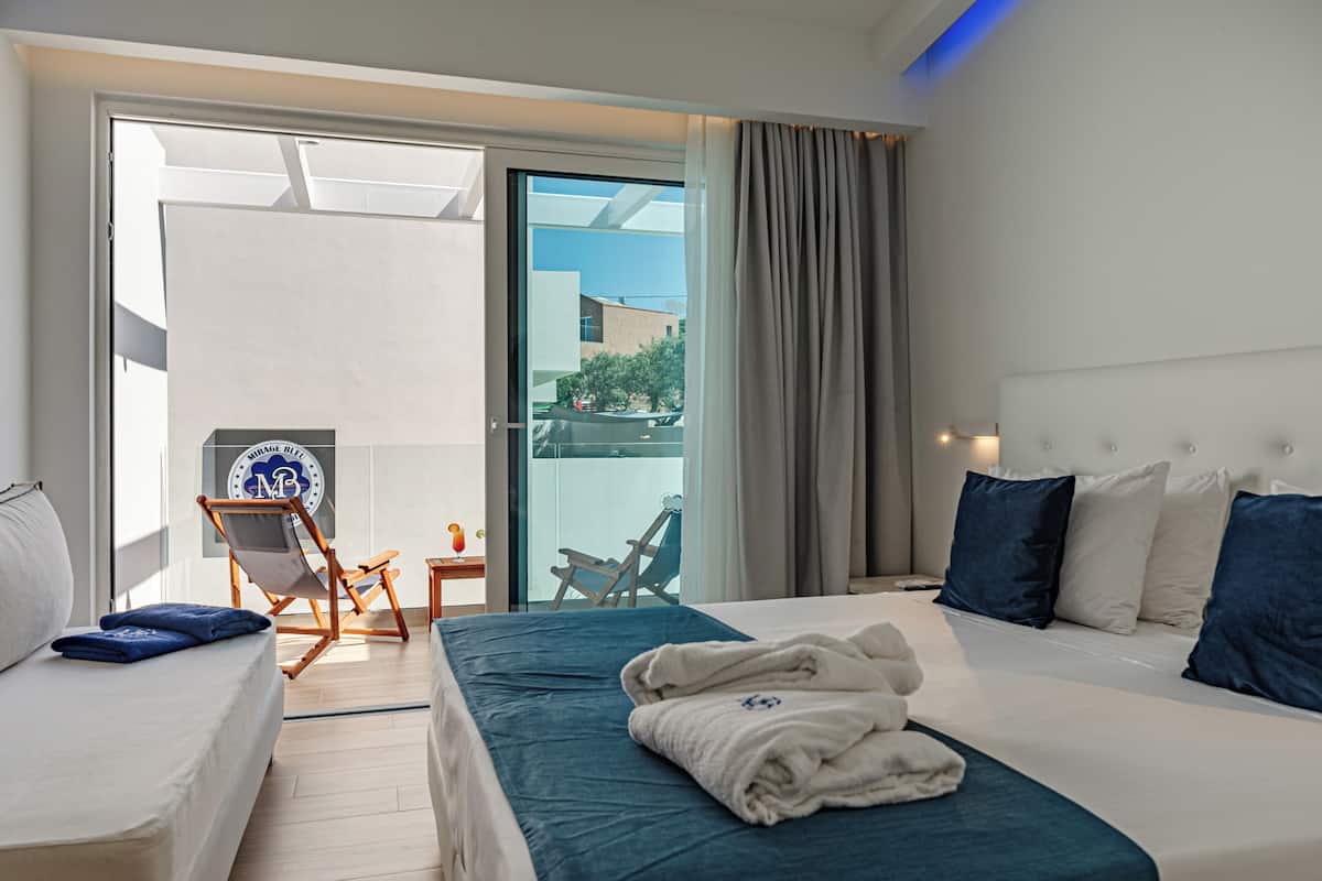 A hotel room with a bed, a chair, a small table, and a view of the outside.