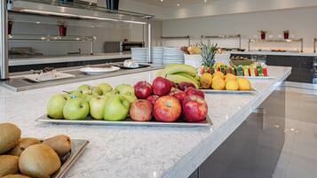 A buffet with various fruits and vegetables, including apples, bananas, and pineapples, arranged on a marble countertop.