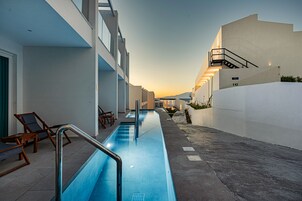 A pool area with a long, narrow pool, lounge chairs, and a staircase leading to an upper level.