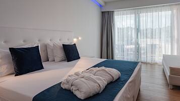 Una camera d'albergo moderna con un letto grande, un comodino e vista sull'esterno attraverso tende leggere.