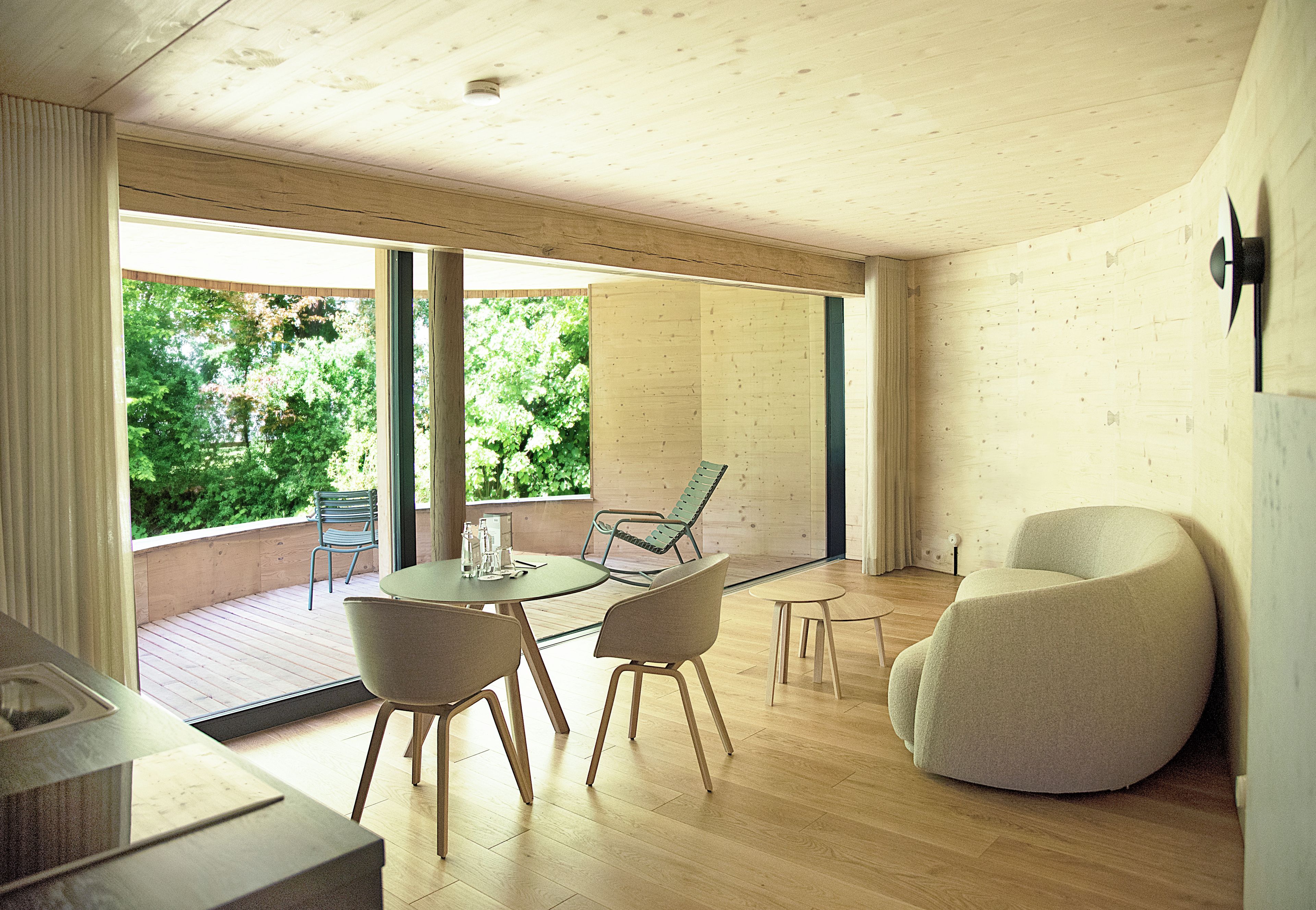 Un intérieur moderne avec un plancher en bois, une table ronde entourée de chaises et une grande fenêtre donnant sur un paysage verdoyant.