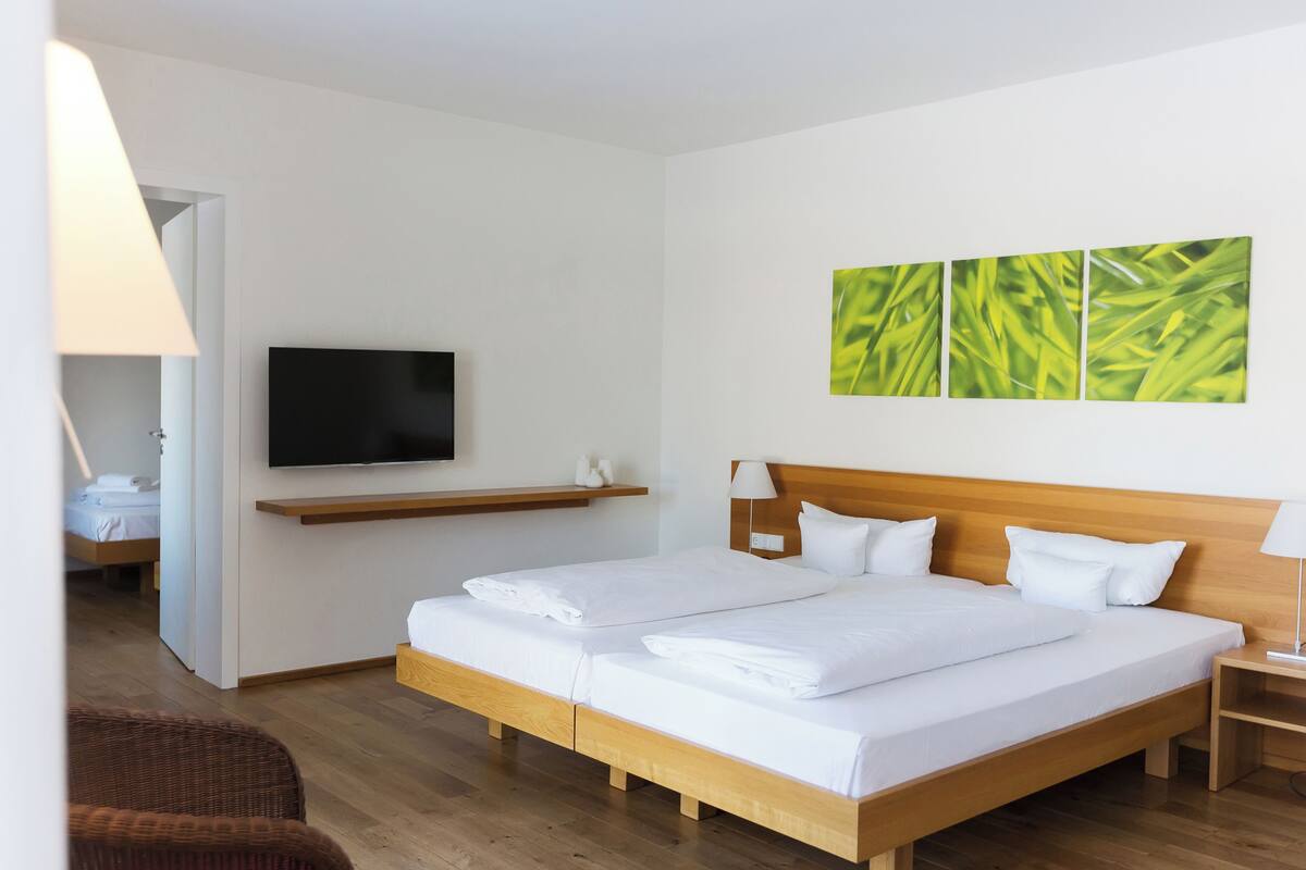 A hotel room with a large bed, a TV mounted on the wall, and a painting above the bed.