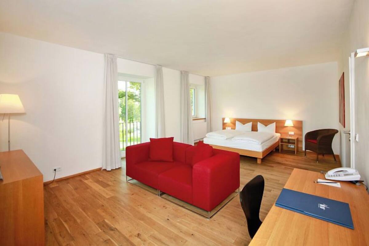 A hotel room with a red sofa, a bed, a desk, and a chair.