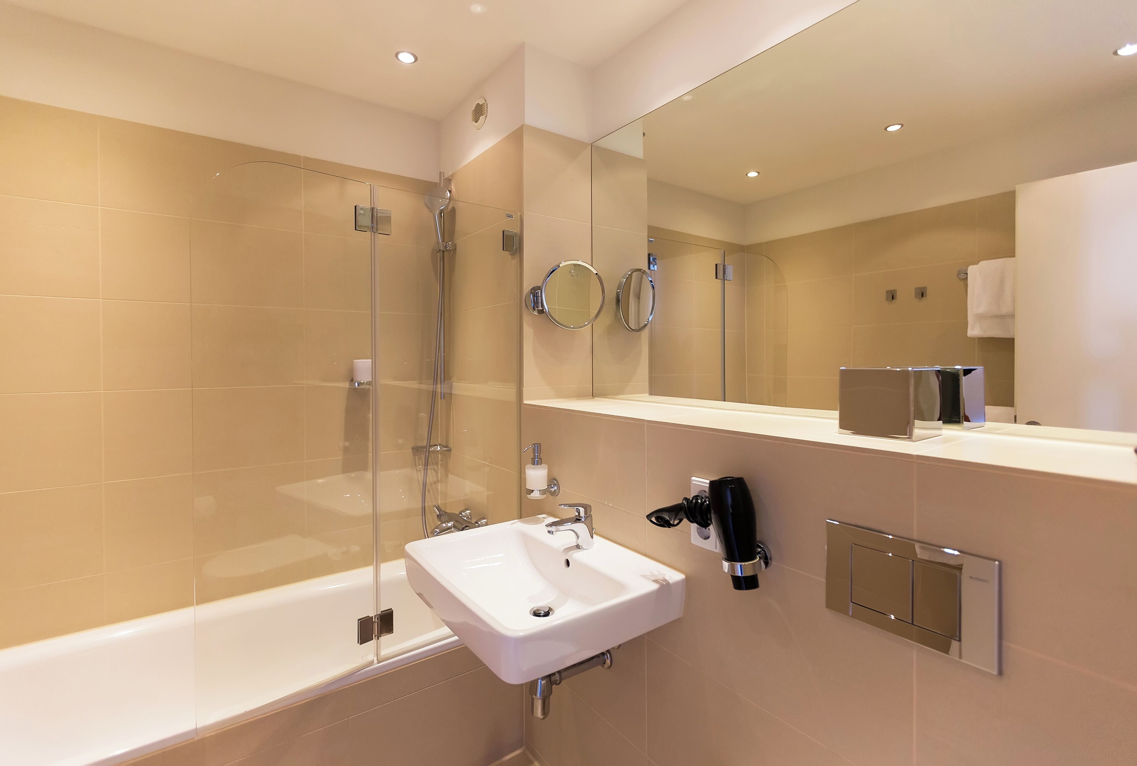 Un baño moderno con ducha envuelta en vidrio, un lavabo blanco y un espejo grande.