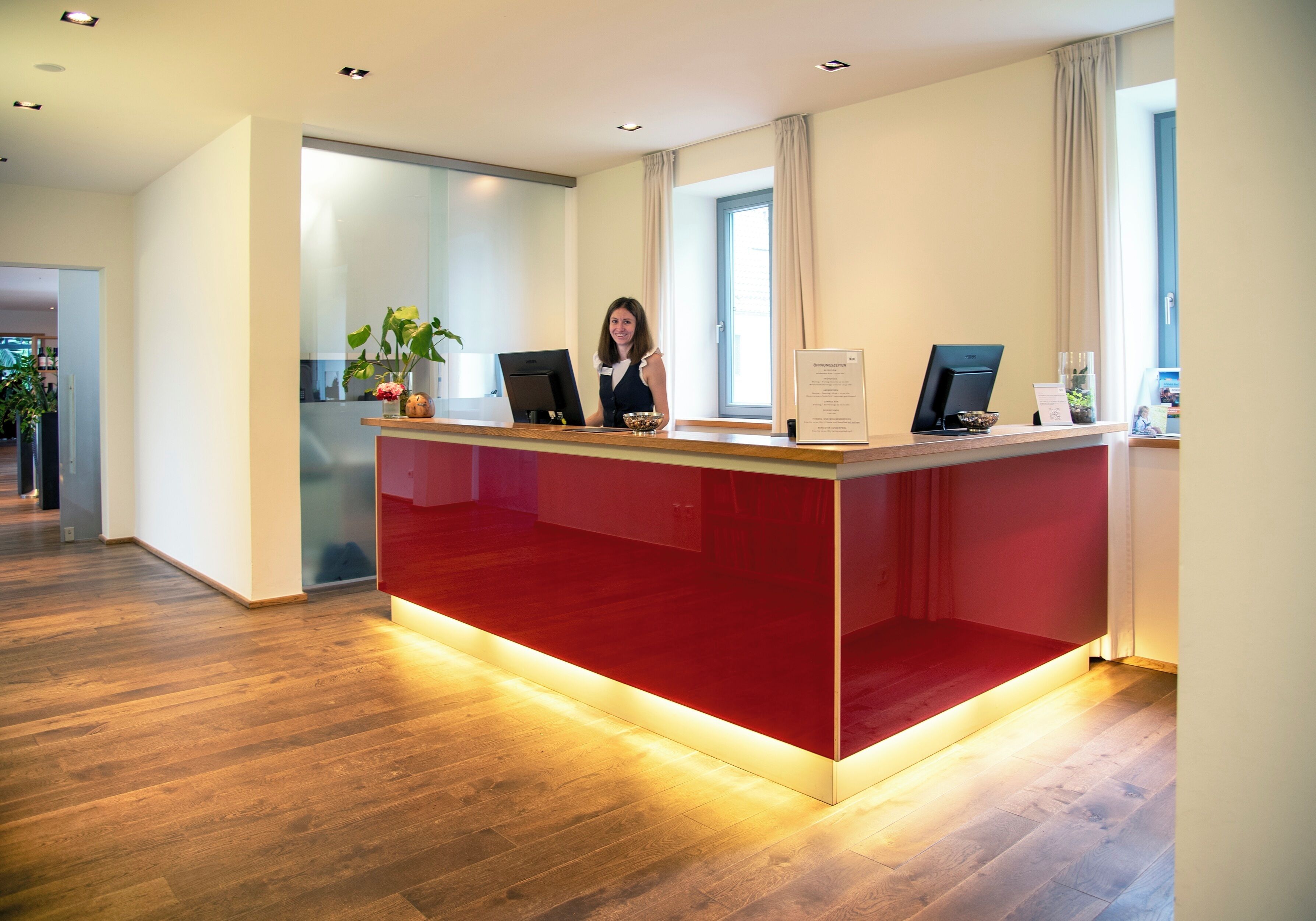Un comptoir d’accueil avec un revêtement rouge, un ordinateur et une plante.