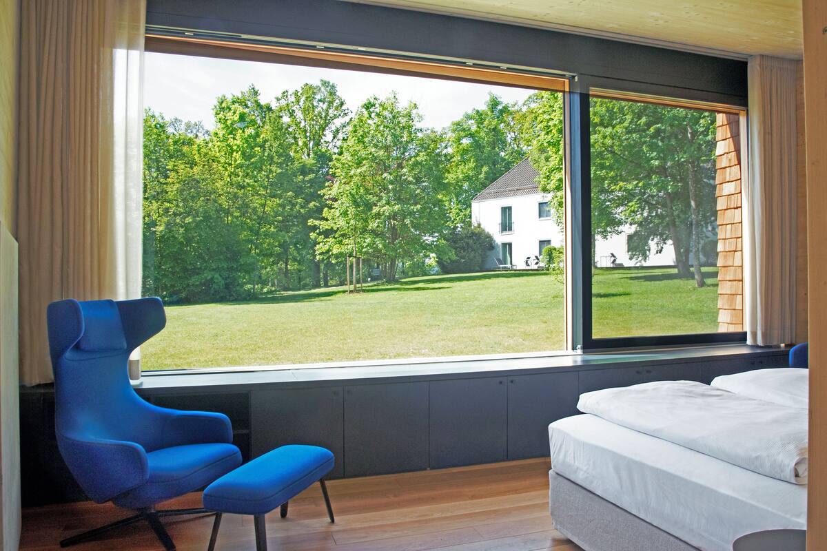 A bedroom with a large window, a blue chair, and a bed.