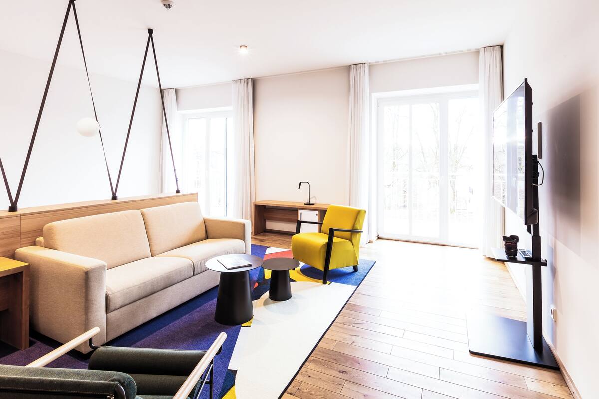 A modern living room with a sofa, a yellow armchair, a TV, and a wooden floor.