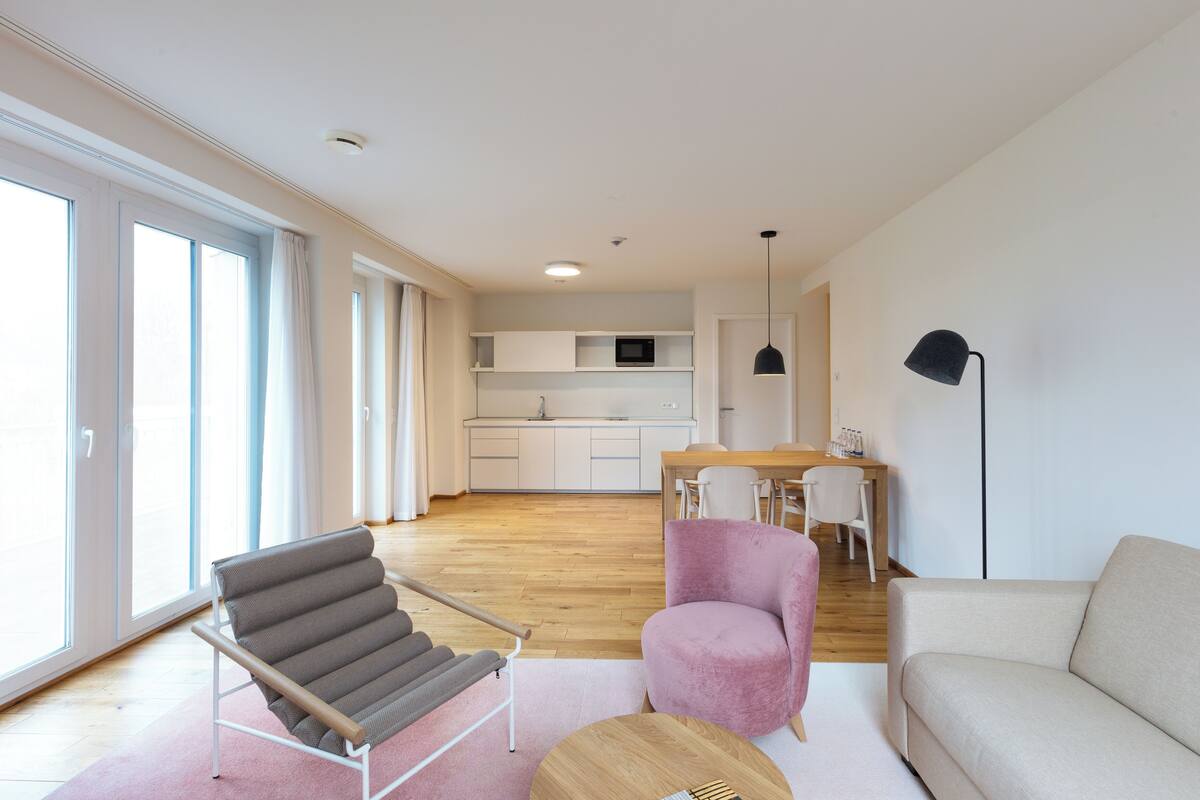 A modern living room with a sofa, a chair, a small table, and a dining area with a table and chairs.