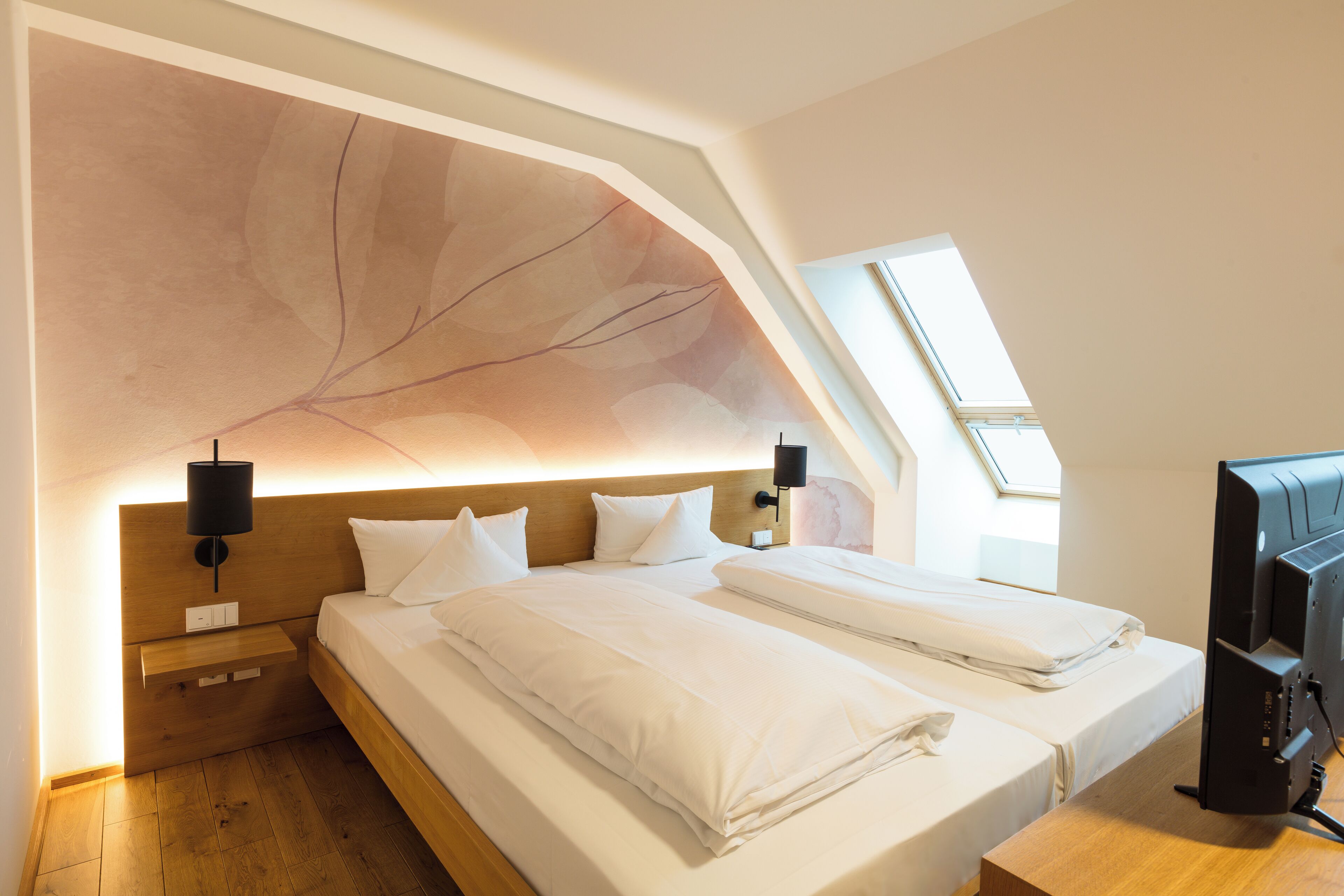 Un dormitorio moderno con techo inclinado, dos camas, un televisor y un tragaluz.