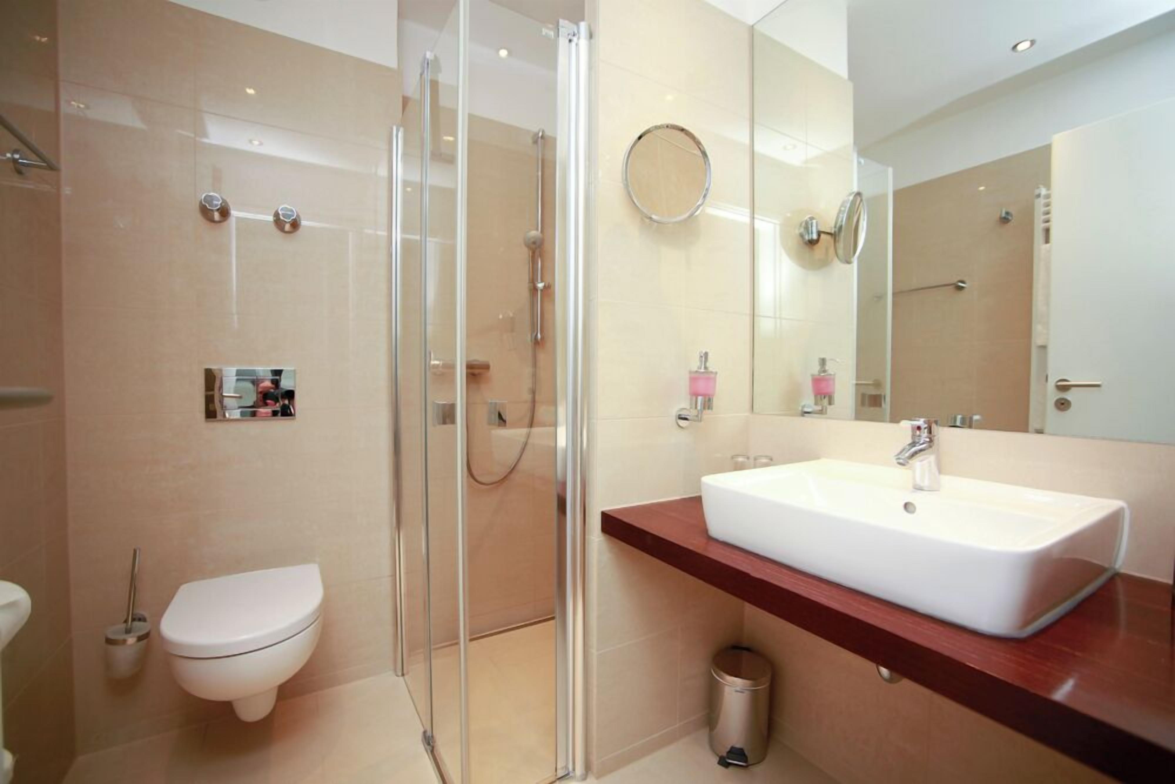 Un baño moderno con cabina de ducha de vidrio, inodoro blanco y tocador con lavamanos blanco.