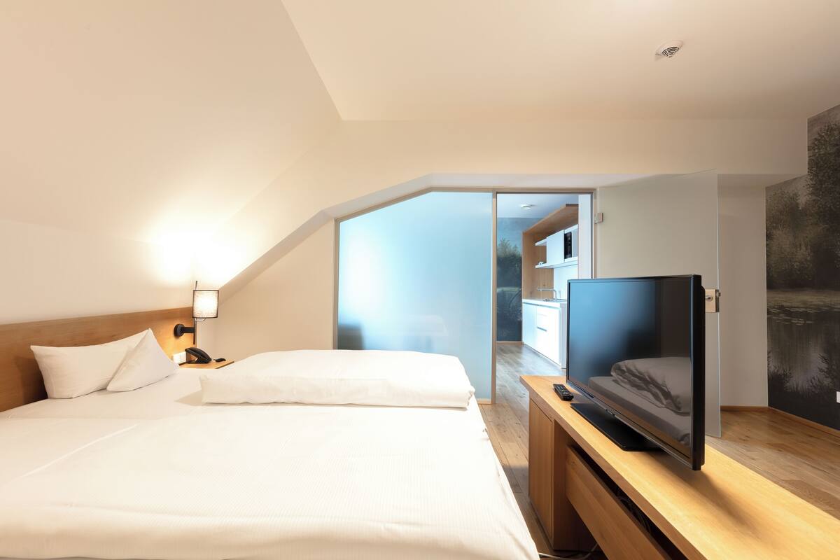 A modern hotel room with a large bed, a flat-screen TV, and a wooden desk.