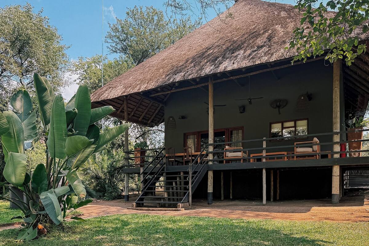 A building with a thatched roof, wooden staircase, and outdoor seating area.