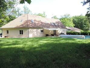 A house with a tiled roof, a covered patio area with outdoor furniture, and a swimming pool.