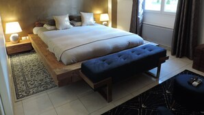 Un dormitorio ordenado con una cama grande, lámparas de noche, un banco y vistas al exterior a través de una ventana.