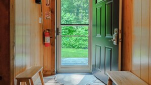 A wooden cabin interior with an exit door leading outside, a fire extinguisher, and a bench. - 2Q Cabin near Leesville Lake ~Pets welcome~ (Carrollton)