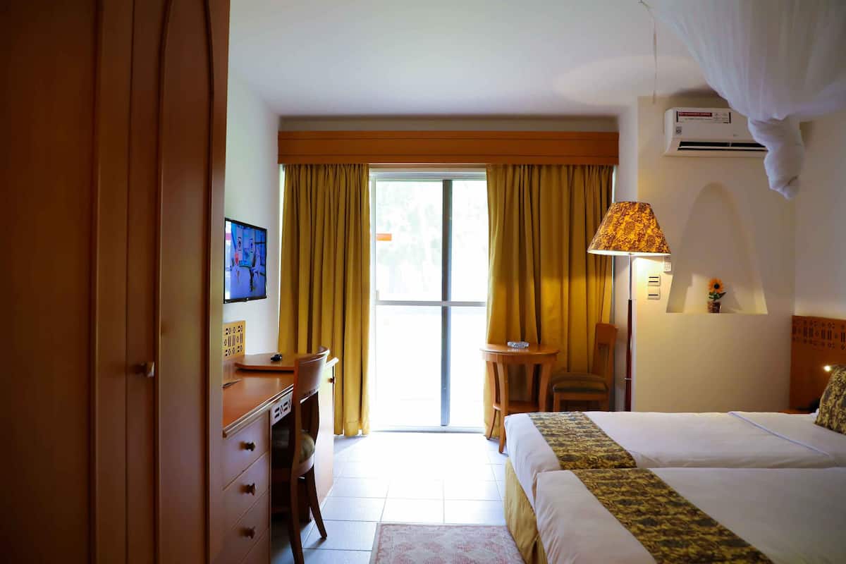 Une chambre d’hôtel avec un lit, un bureau et une chaise, une télévision et une fenêtre avec des rideaux.