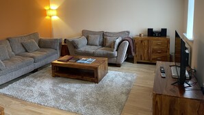Una sala de estar con dos sofás grises, una mesa de centro de madera, un televisor sobre un mueble de madera y una lámpara.