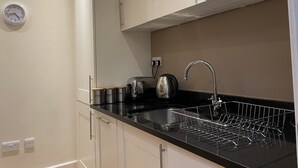 Una cocina moderna con armarios blancos, encimera negra, pileta de acero inoxidable y hervidor.