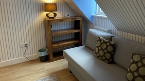 Un dormitorio tipo loft acogedor con techo inclinado, una estantería de madera, un sofá con cojines estampados y una mesita de noche con lámpara.