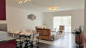 Een ruime woonkamer met een eettafel voor vier personen, een bank en een salontafel. Een groot raam zorgt voor natuurlijk licht en uitzicht op buiten.