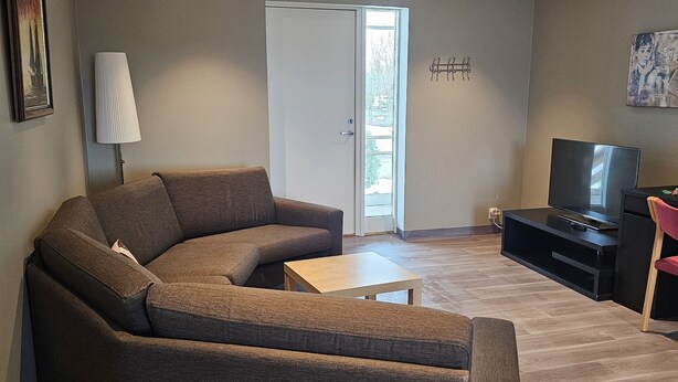 A living room with a sectional sofa, a coffee table, a TV, and a door leading to a balcony. - Solvoll (Tønsberg)