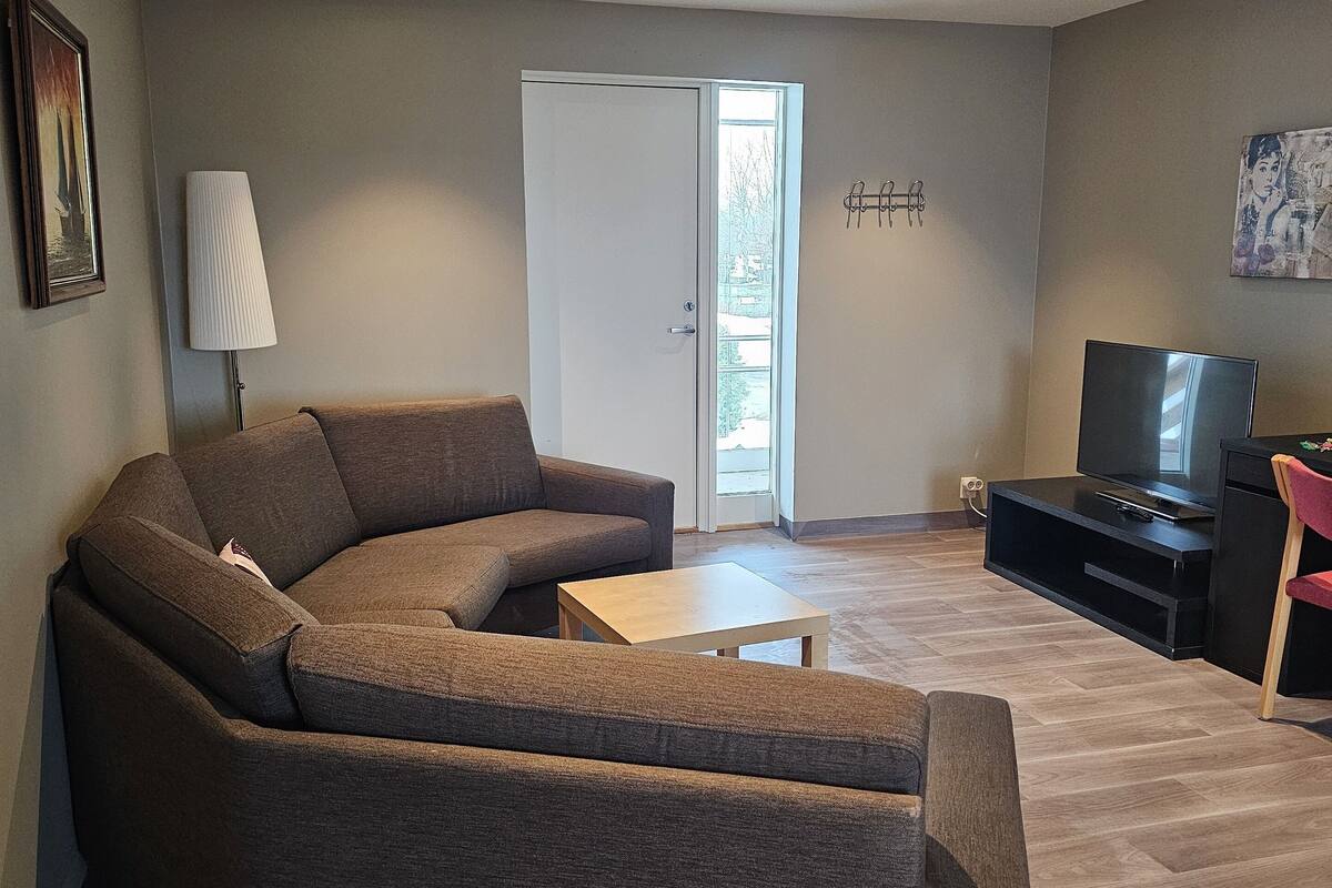 A living room with a sectional sofa, a coffee table, a TV, and a door leading to a balcony.