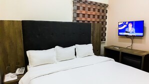 A hotel room with a large bed, a TV on a stand, a phone on the nightstand, and an air conditioner on the wall. - Come Inn Hotel (Abuja)