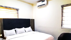 A hotel room with a bed, a chair, an air conditioning unit, and a window with blinds. - Come Inn Hotel (Abuja)