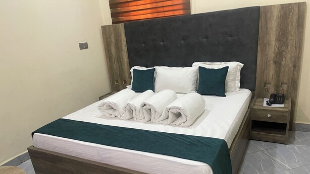 A neatly made bed with a dark headboard, white linens, and teal pillows. - Come Inn Hotel (Abuja)