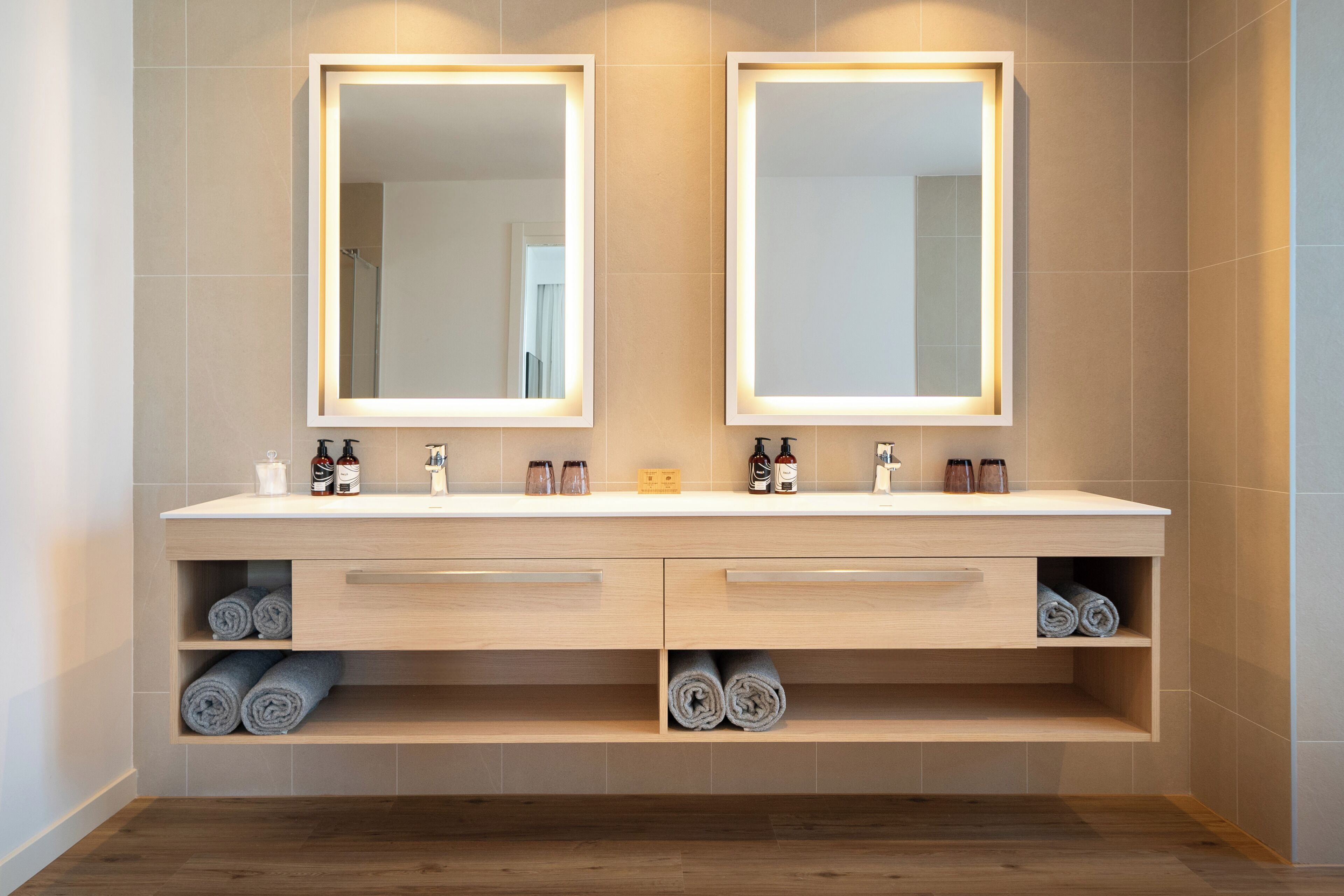 Un baño moderno con tocador doble, dos espejos y repisas empotradas para toallas.