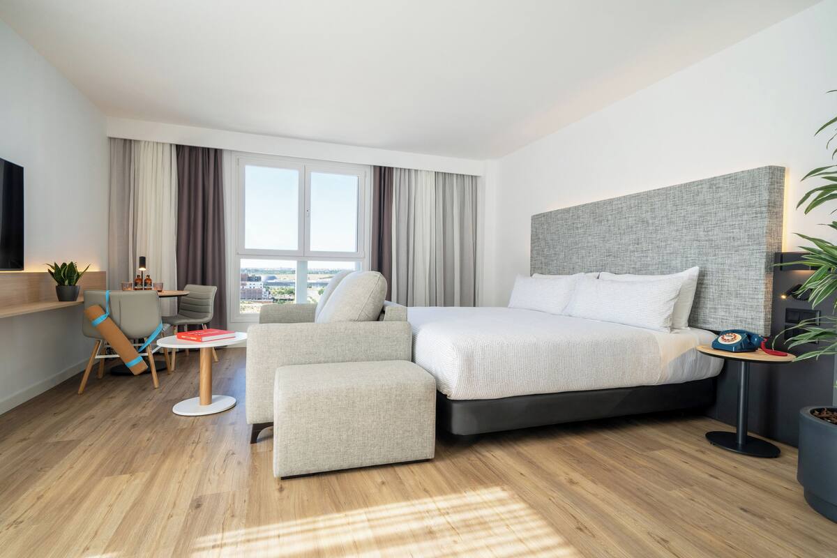A modern hotel room with a large bed, a sofa, a small table, and a TV.