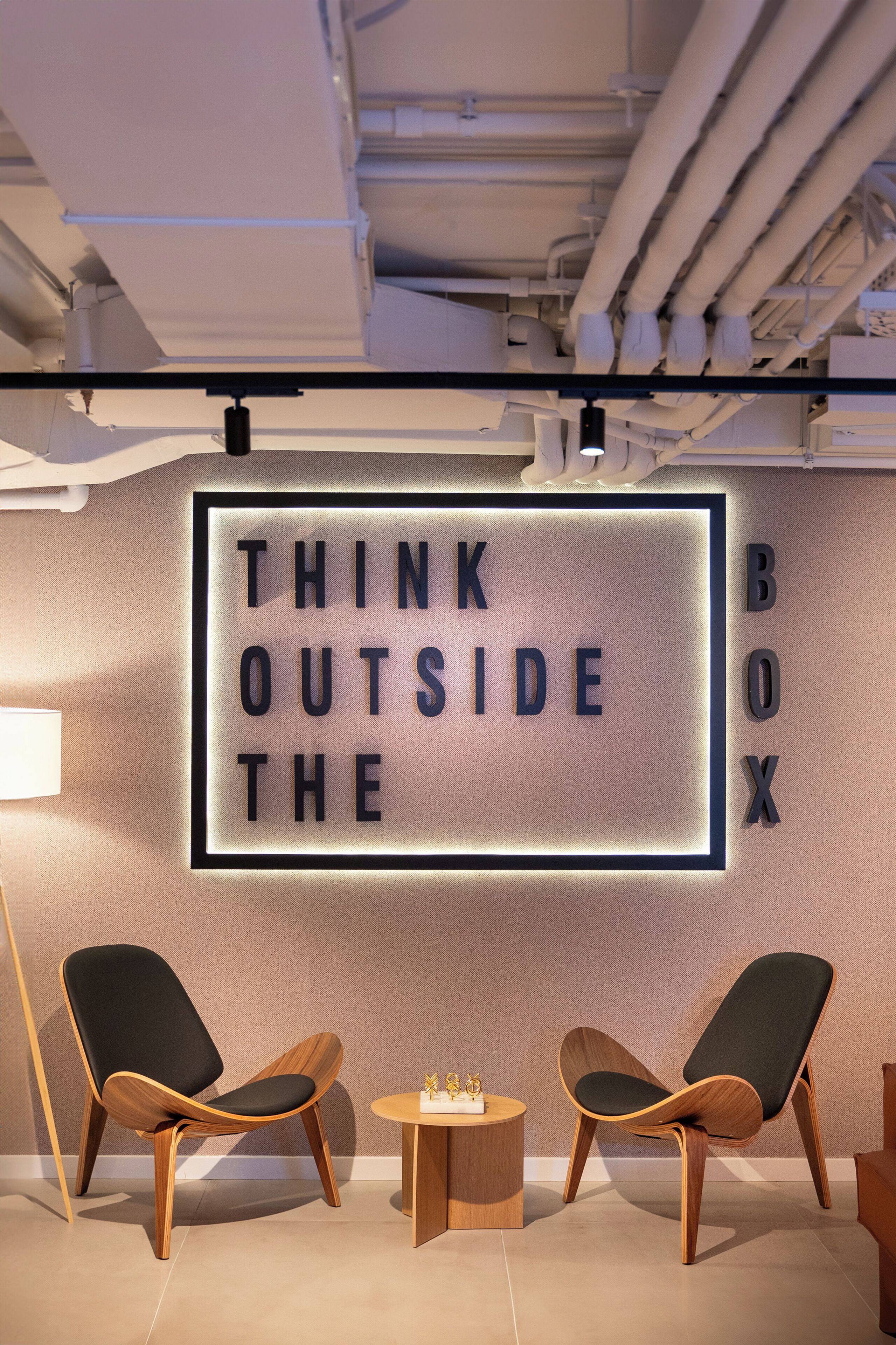 Ein modernes Interieur mit einem motivierenden Wandspruch, zwei Holzstühlen und einem kleinen runden Tisch.