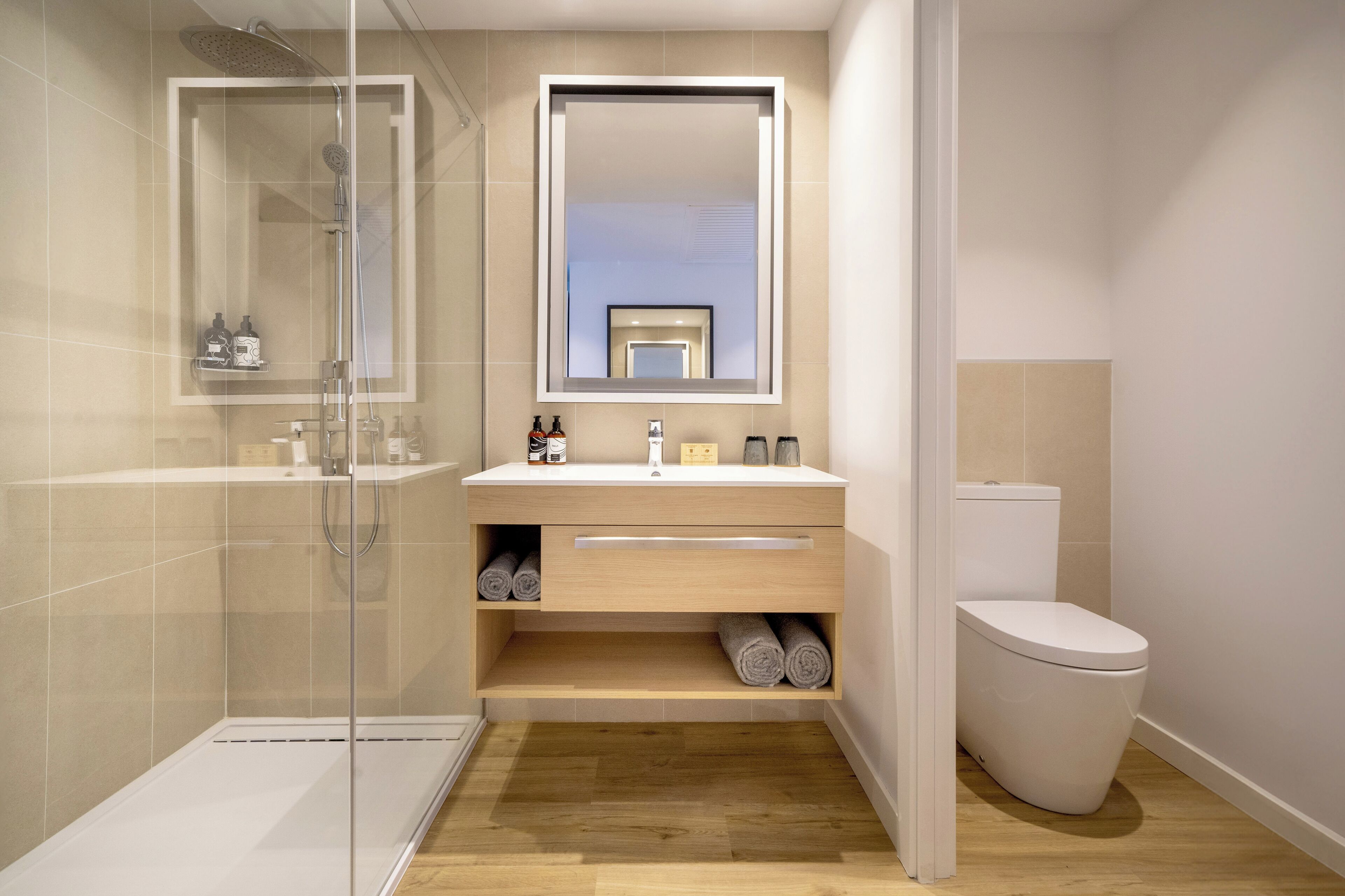 Un baño moderno con ducha envuelta en vidrio, tocador de madera con espejo y un inodoro.