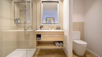 Un baño moderno con ducha envuelta en vidrio, tocador de madera con espejo y un inodoro.