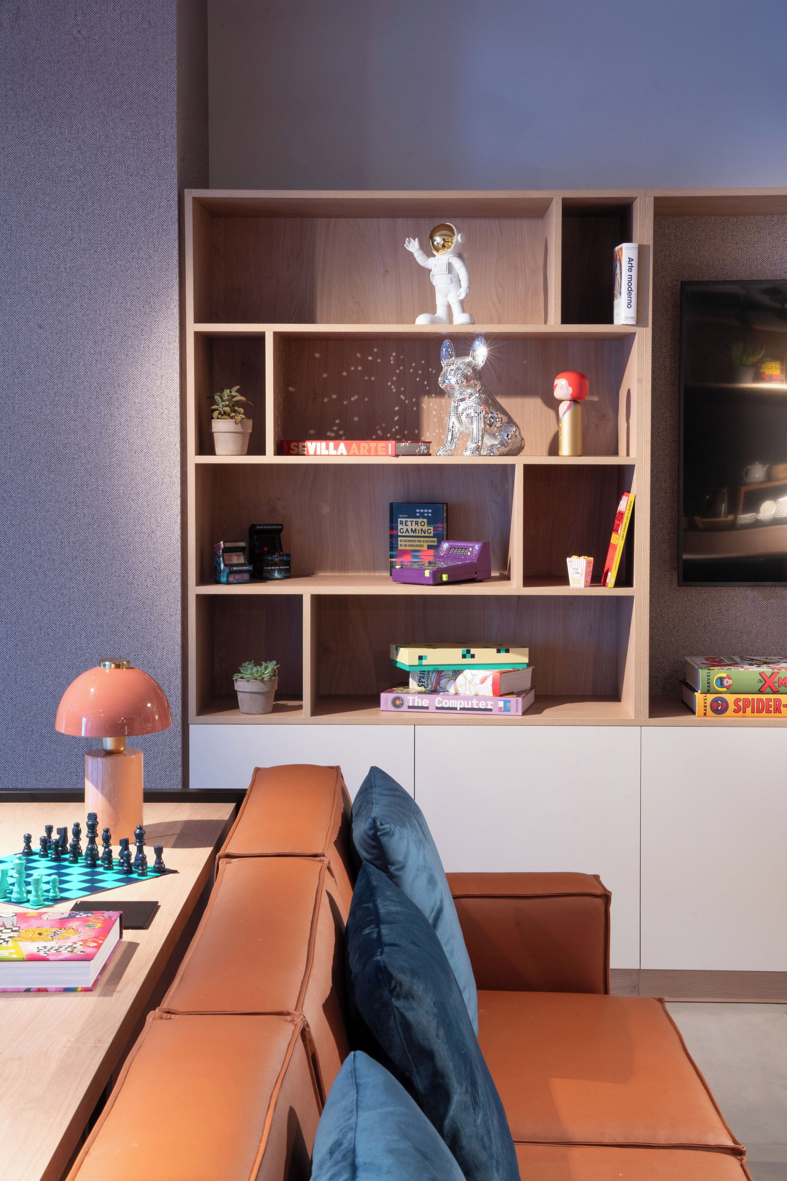 Una sala de estar moderna con una estantería de madera, una consola de videojuegos y un tablero de ajedrez.