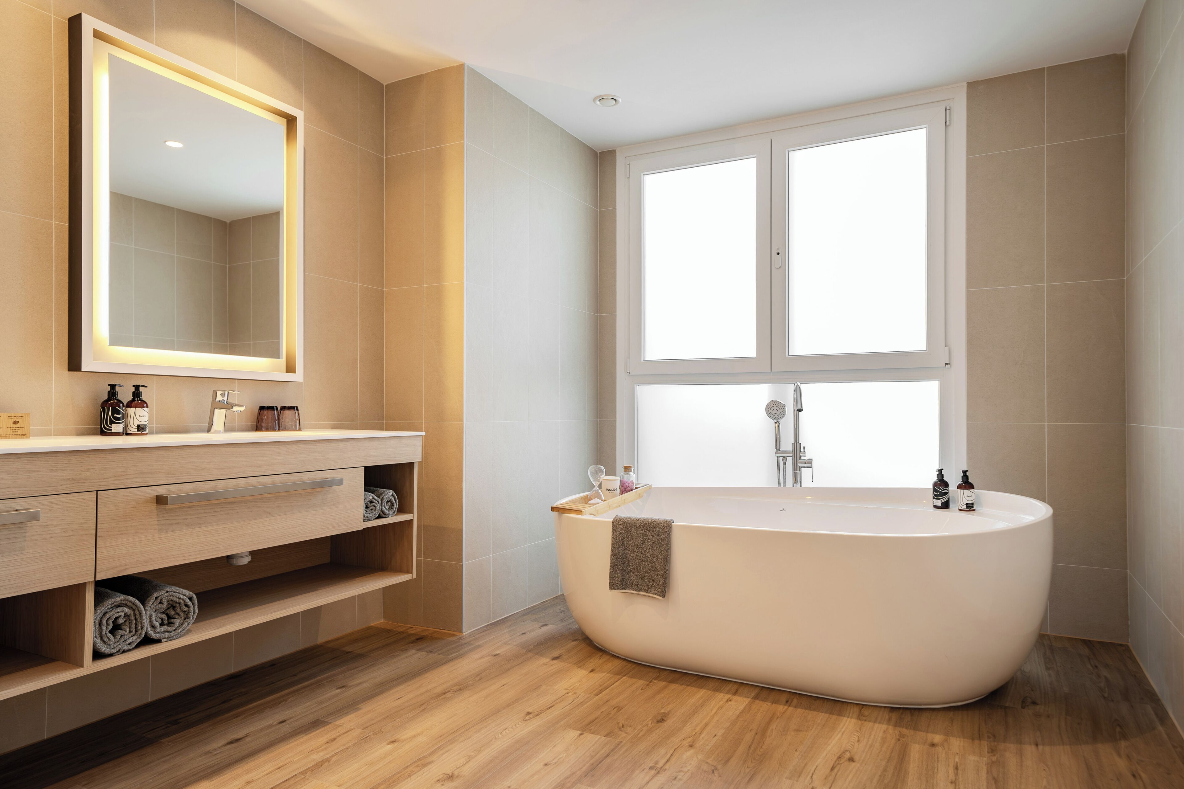 A modern bathroom with a freestanding bathtub, a large mirror, and a window providing natural light.