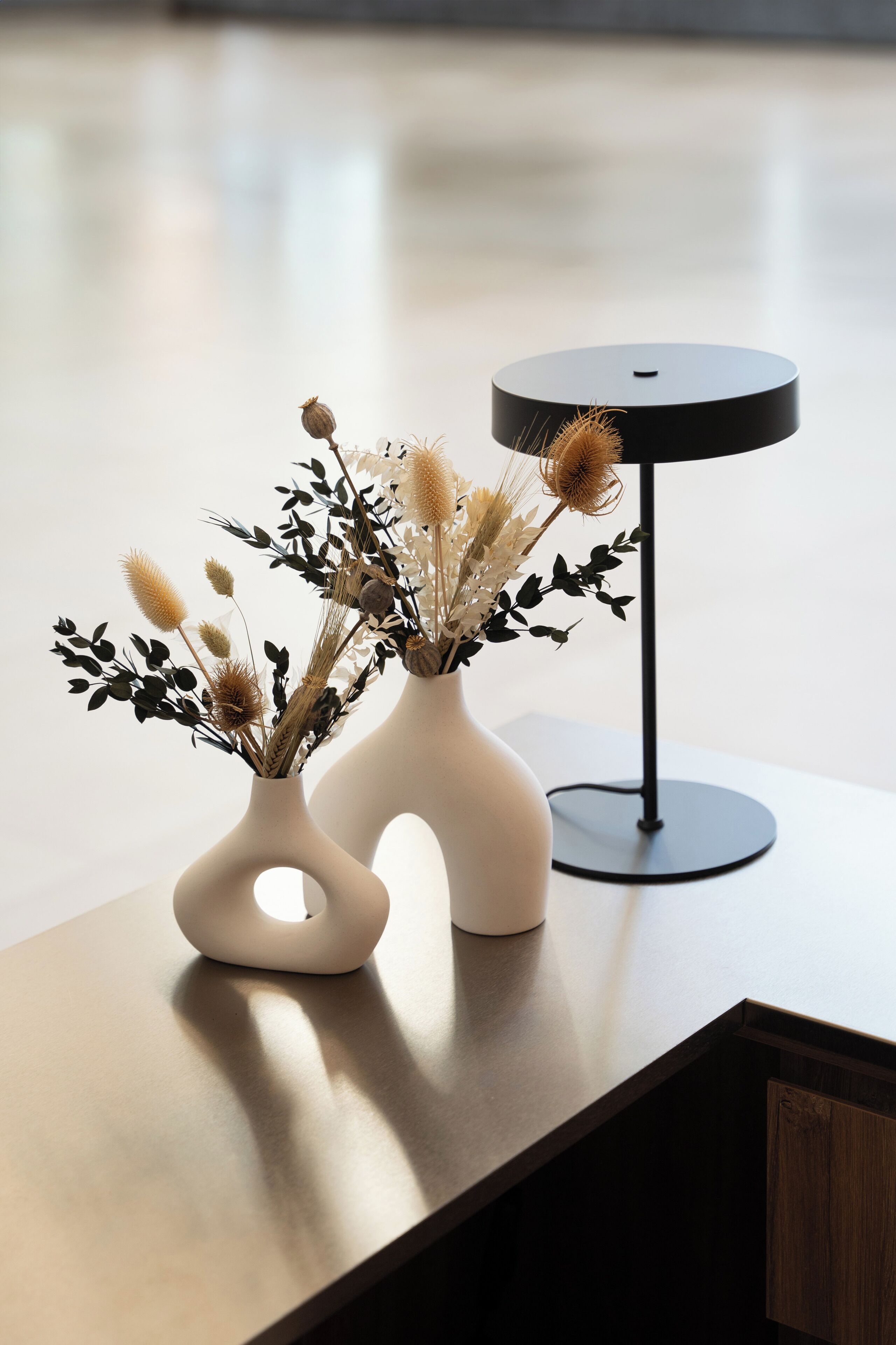 Dos jarrones blancos con flores secas sobre una mesa de madera.
