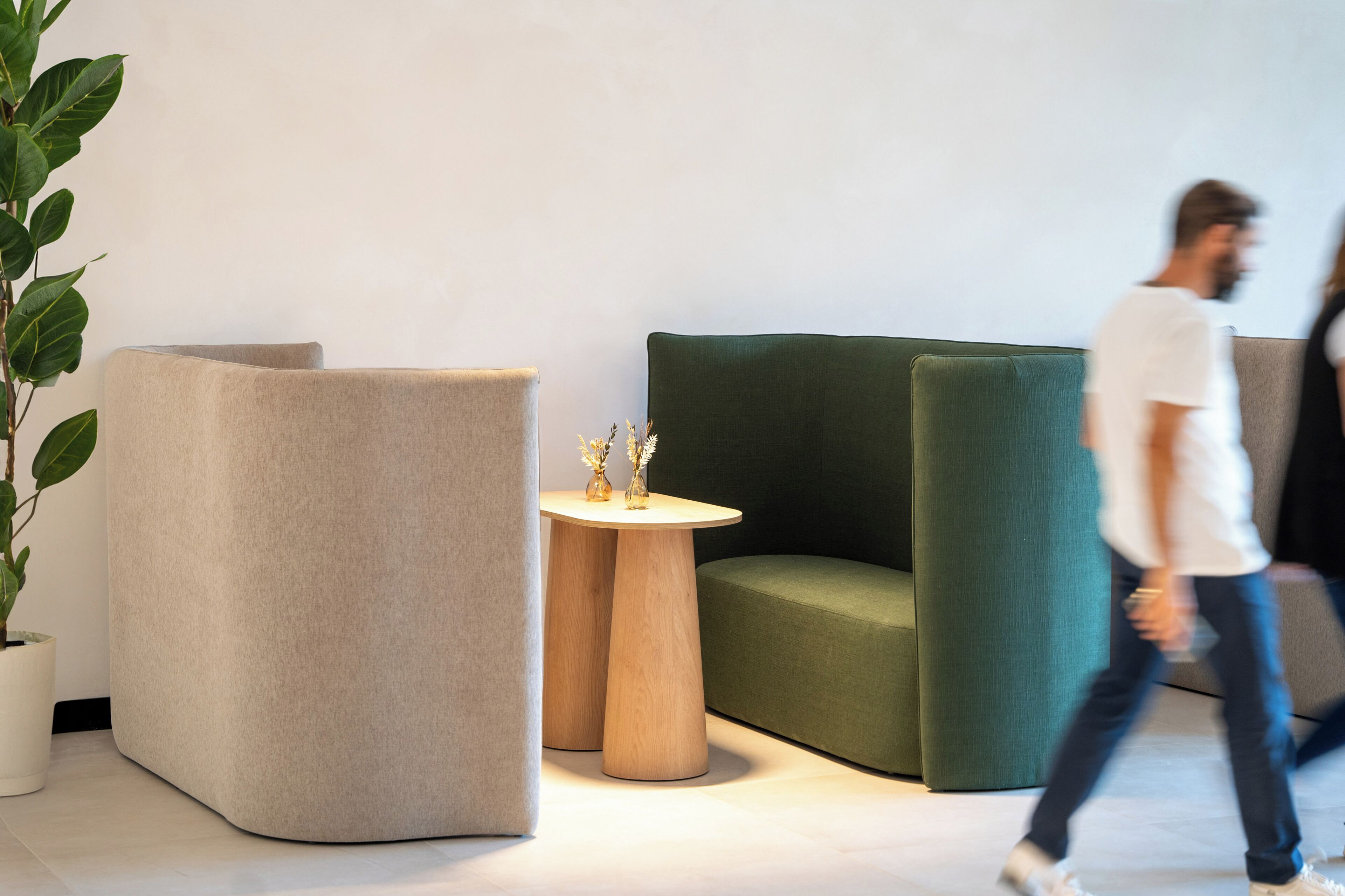 Un interior moderno con un sofá verde, un sillón beige y una pequeña mesa de madera con objetos decorativos.