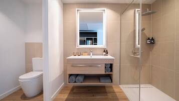 Un baño moderno con inodoro, lavamanos con espejo, ducha y suelo de madera.