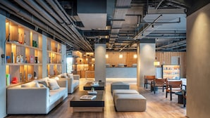 A modern lounge area with sofas, a coffee table, and a bookshelf filled with books and decorative items. - INNSiDE by Meliá Madrid Valdebebas (Madrid)