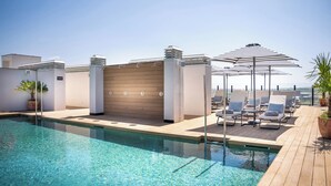A rooftop pool with lounge chairs and umbrellas, surrounded by a wooden deck and a white wall with a gate. - INNSiDE by Meliá Madrid Valdebebas (Madrid)
