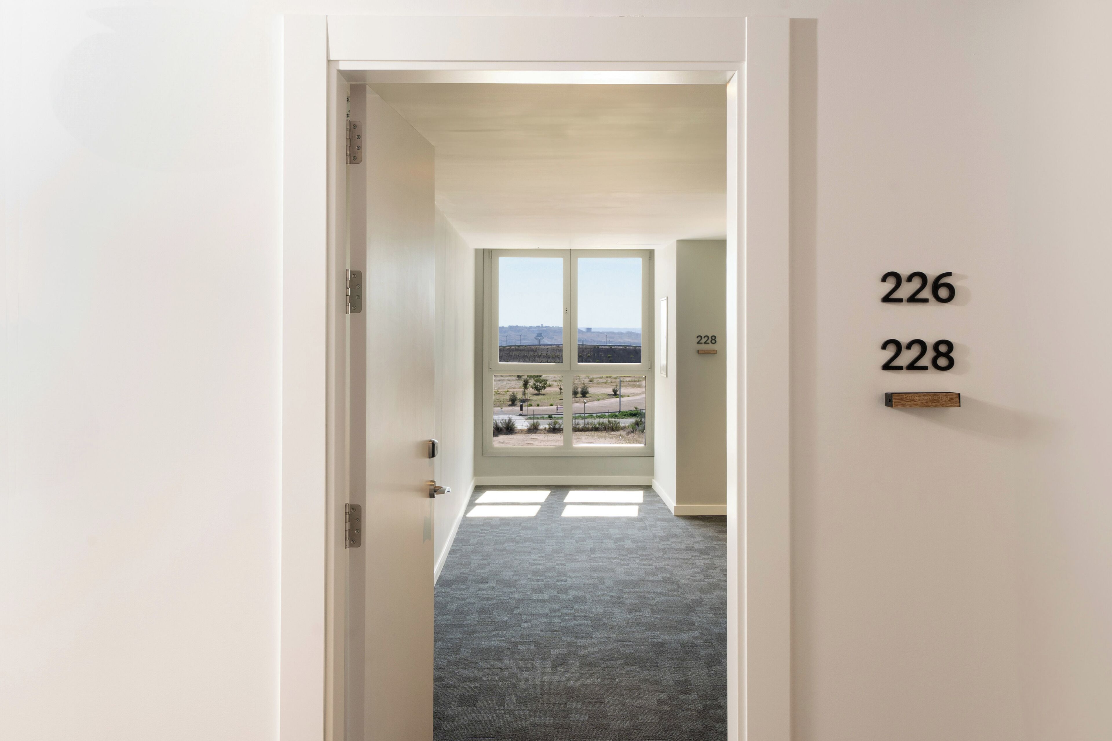 A hallway with a carpeted floor leading to a door marked with numbers 226 and 228.