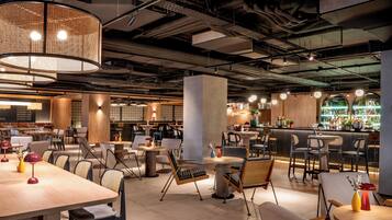 Un restaurante moderno con varias zonas de estar, incluyendo mesas redondas y cabinas, además de una zona de bar con diversas opciones de asientos.